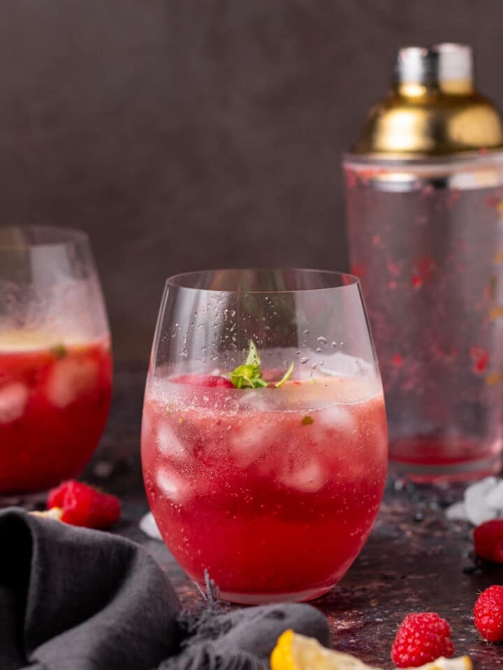 Fizzy cocktail served over ice with fresh berries and lemon nearby.
