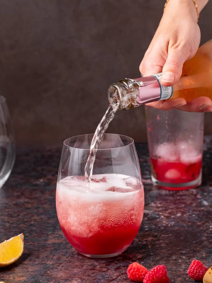 Prosecco being poured into a pink gin cocktail over ice to create a gin fizz.