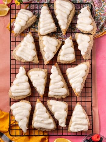 Overhead view of frosted lemon poppyseed scones arranged on a cooling rack with lemon wedges and berries.