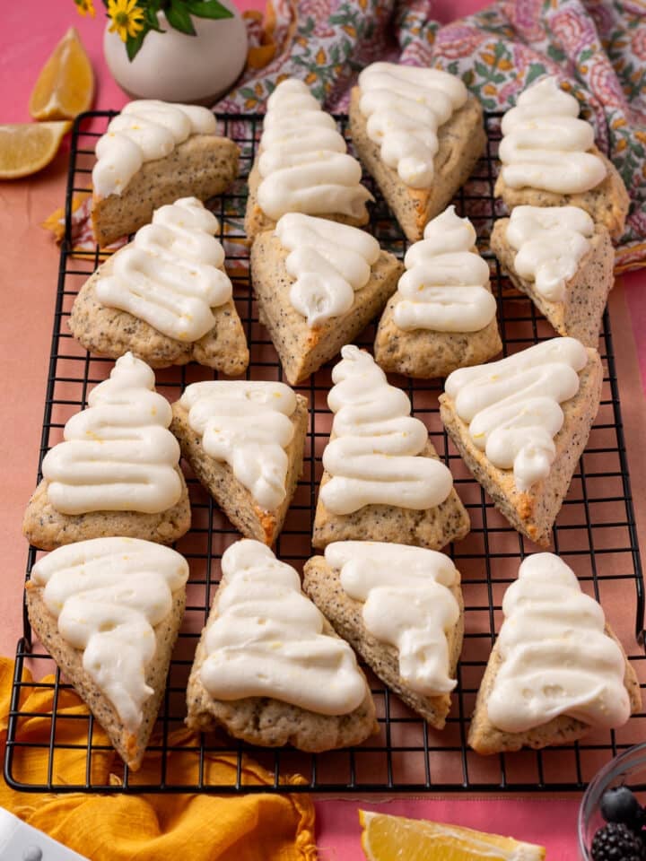 Frosted lemon poppyseed scones arranged on a black cooling rack with lemon wedges nearby.