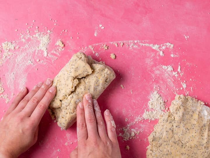 Hands folding lemon poppyseed scone dough into thirds on a lightly floured surface.