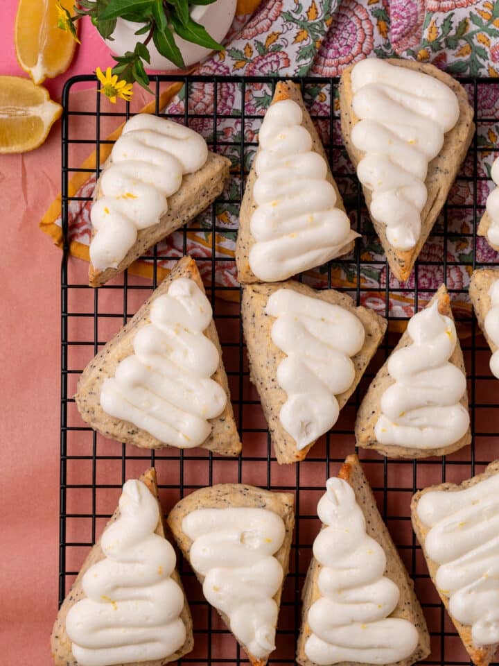 Overhead view of frosted lemon poppyseed scones on a wire rack with a floral cloth and lemon wedges.