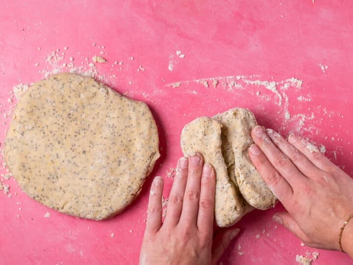 Hands folding one portion of lemon poppyseed scone dough beside a flattened round of dough.