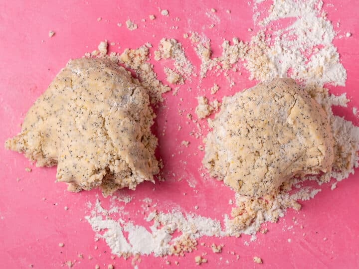 Lemon poppyseed scone dough divided into two portions on a floured pink surface.