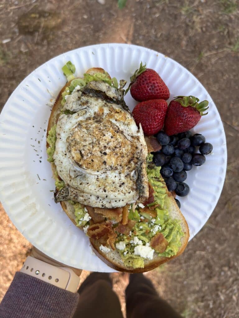 paper plate with bacon avocado toast with a fried egg on top and fresh berries on the side