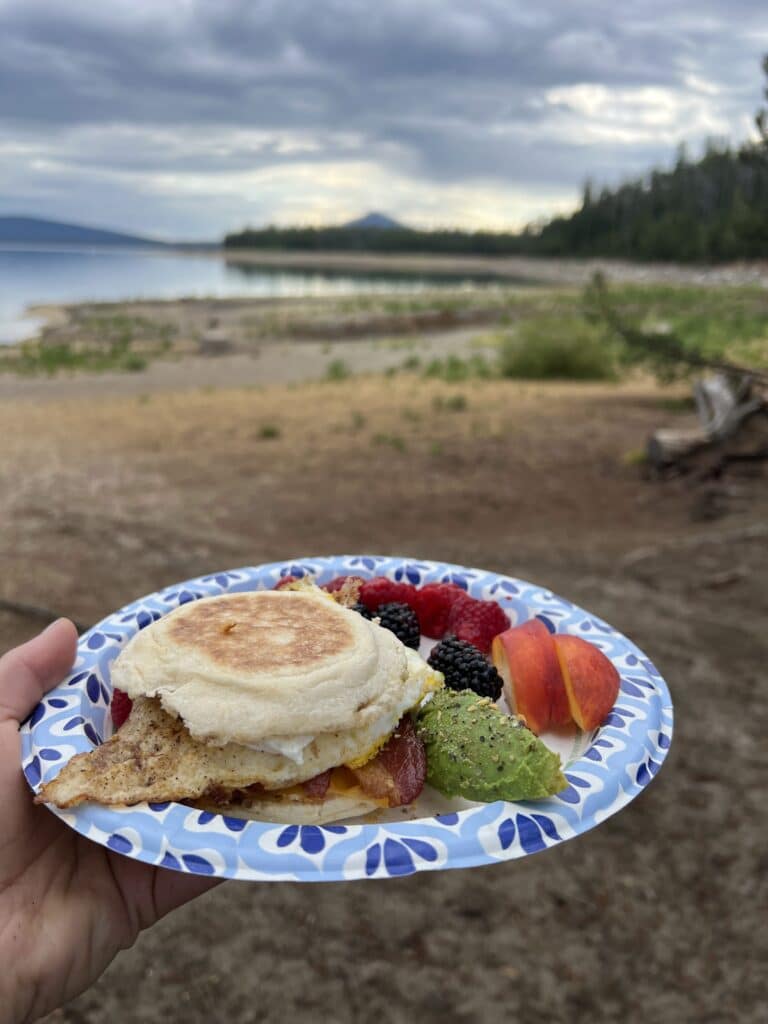 Bacon, egg, and cheese breakfast sandwich with avocado and fresh fruit on the side
