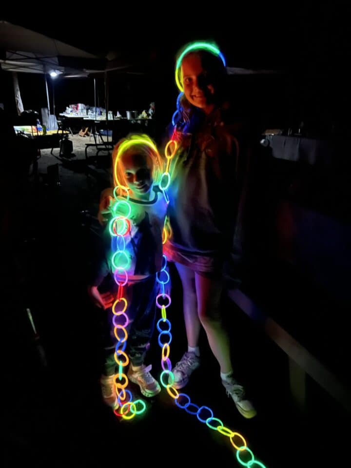 two kids using glow sticks as necklaces, bracelets and crowns in the dark