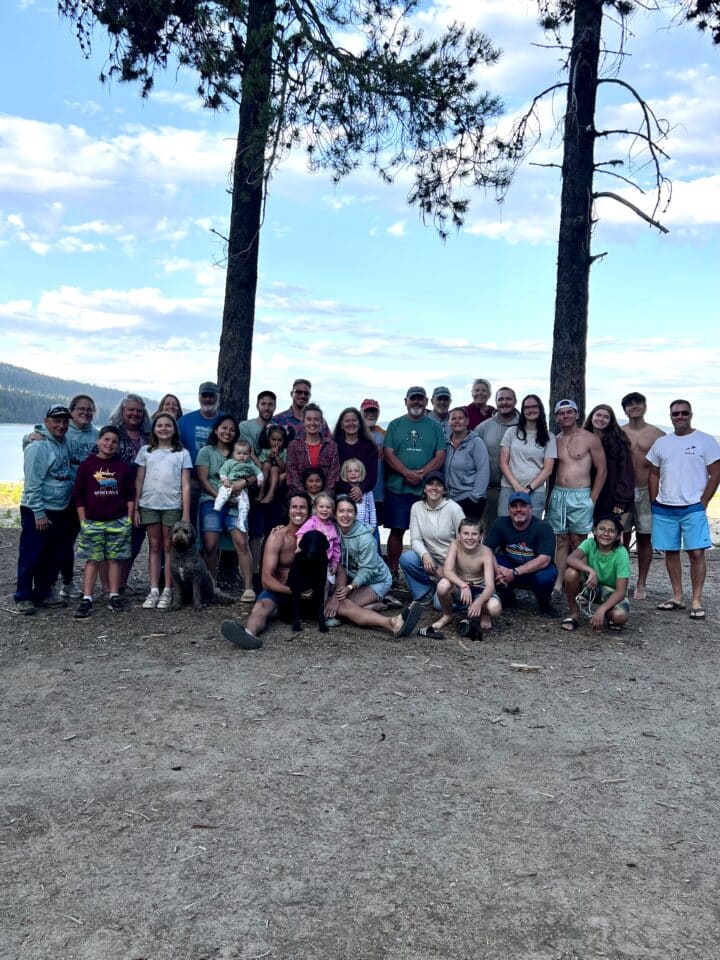 large family grouped in front of two trees and lake at a campsite