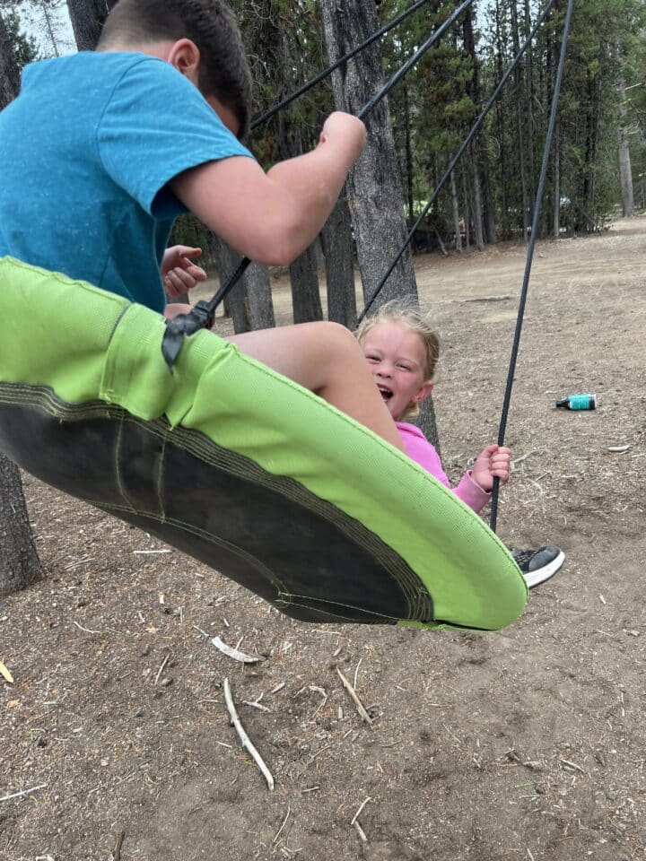 two children swinging on a saucer tree swing