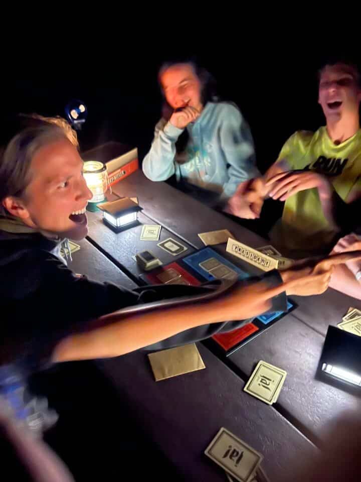 three people sitting around a picnic table at night playing a board game