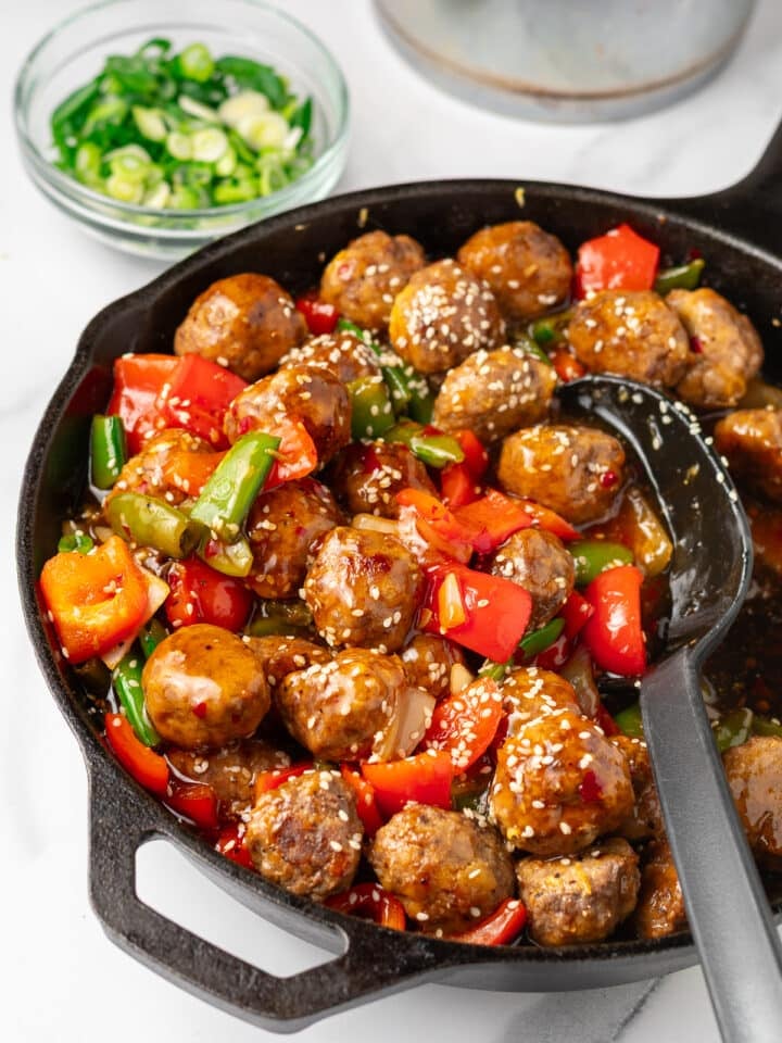 Meal prep meatballs with sweet chili sauce, sesame seeds, and colorful stir-fry vegetables in a cast-iron skillet.