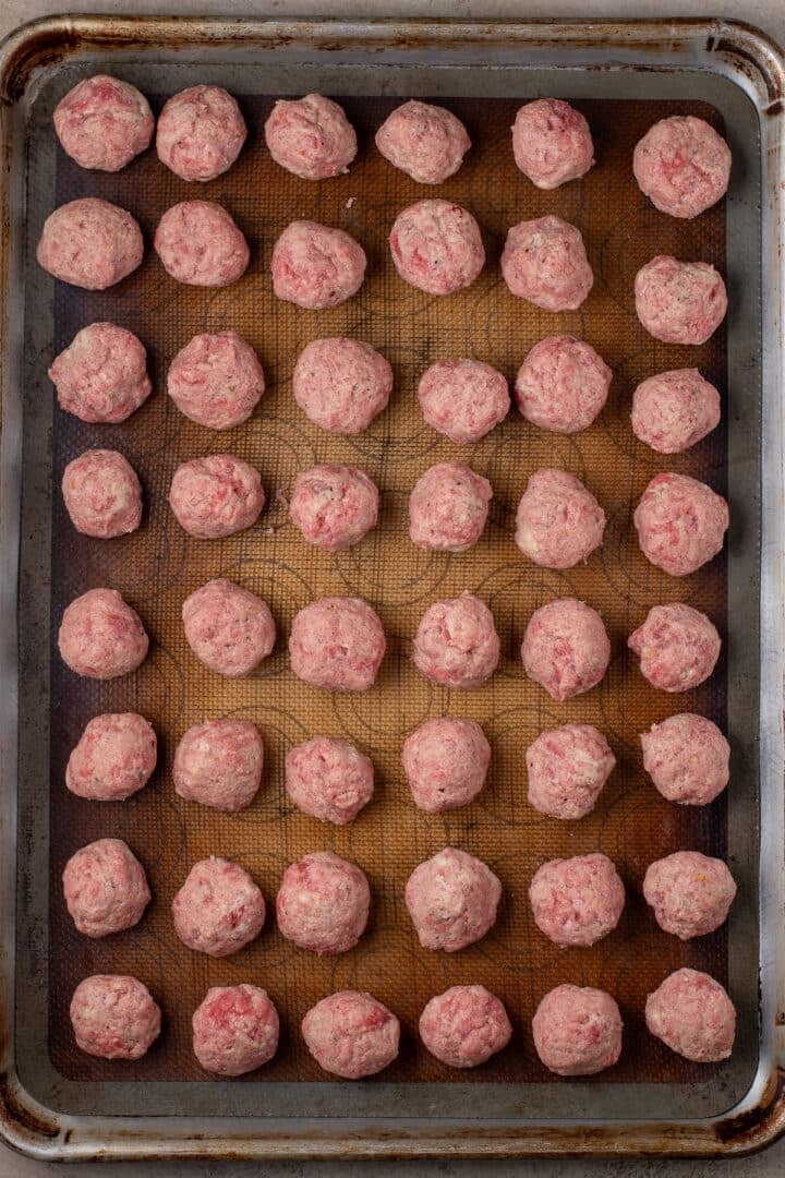 Raw meal prep meatballs arranged on a lined baking sheet.