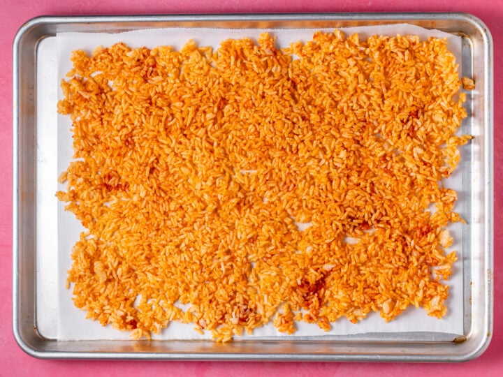 Red curry rice spread in an even layer on a parchment-lined baking sheet