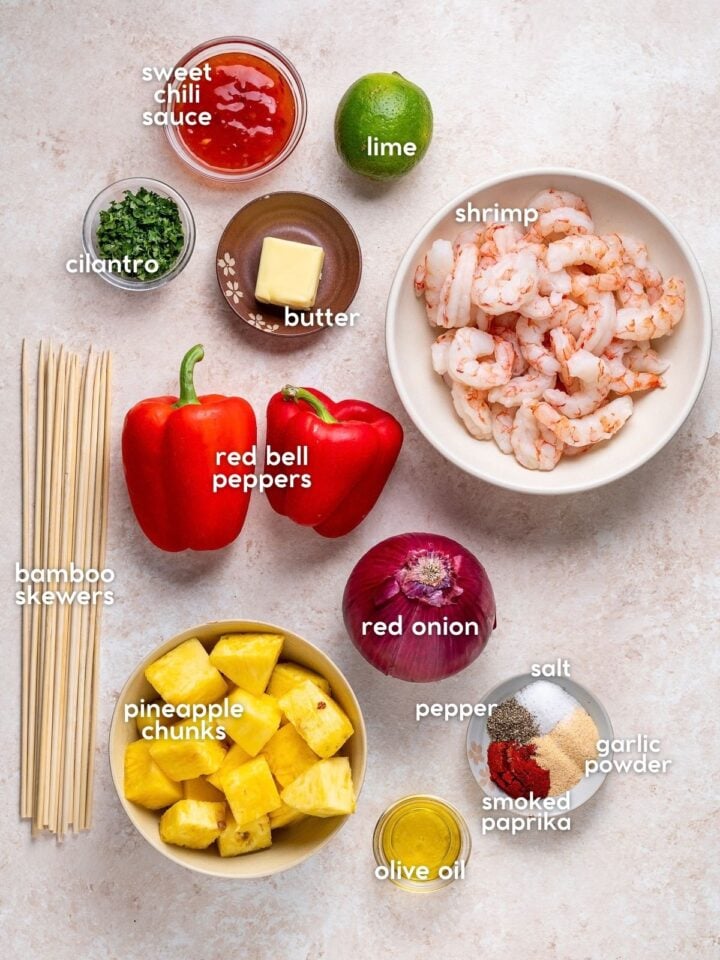 Ingredients for pineapple and shrimp skewers including shrimp, fresh pineapple, red bell peppers, red onion, sweet chili sauce, lime, cilantro and seasonings.