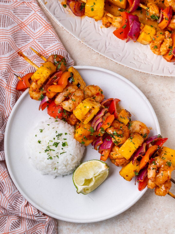Grilled shrimp and veggie skewers served with white rice and lime wedge on a white plate.