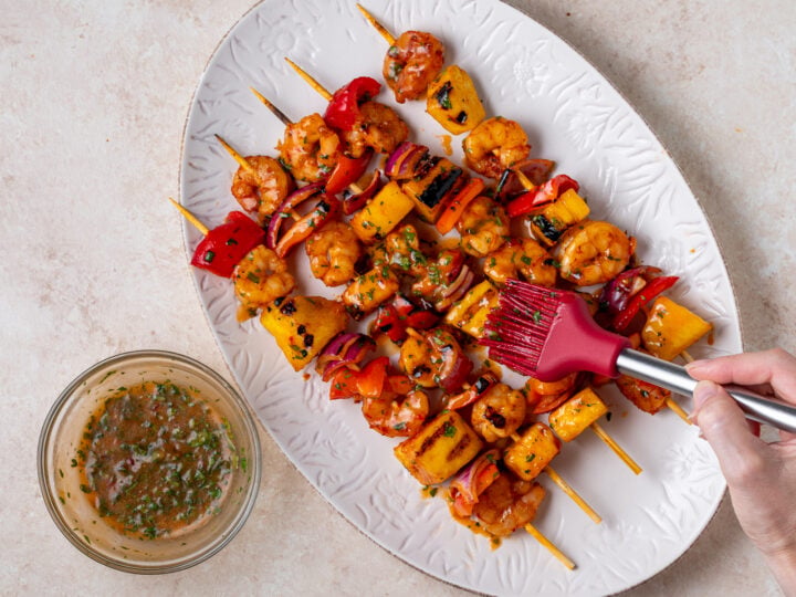 Cilantro sweet chili glaze being brushed over grilled shrimp pineapple skewers.