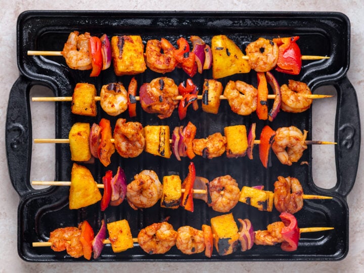 Shrimp and pineapple skewers with red bell pepper and red onion cooking on a cast iron grill pan.