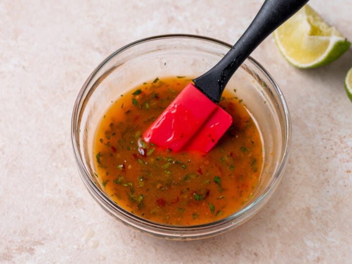 A red spatula mixing cilantro sweet chili glaze in a small glass bowl.
