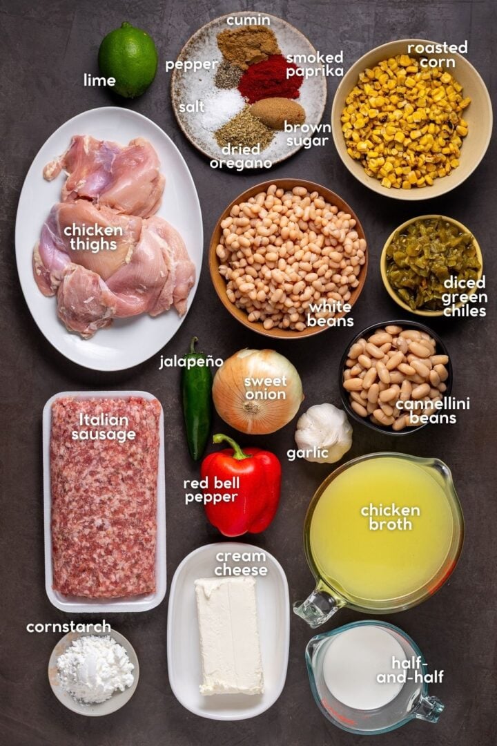 Ingredients for chili with beans including chicken thighs, Italian sausage, white beans, corn, green chiles, peppers, cream cheese and spices.
