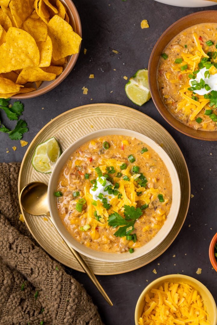 Bowls of creamy chicken chili served with tortilla chips, lime, cilantro, shredded cheese and green onions.