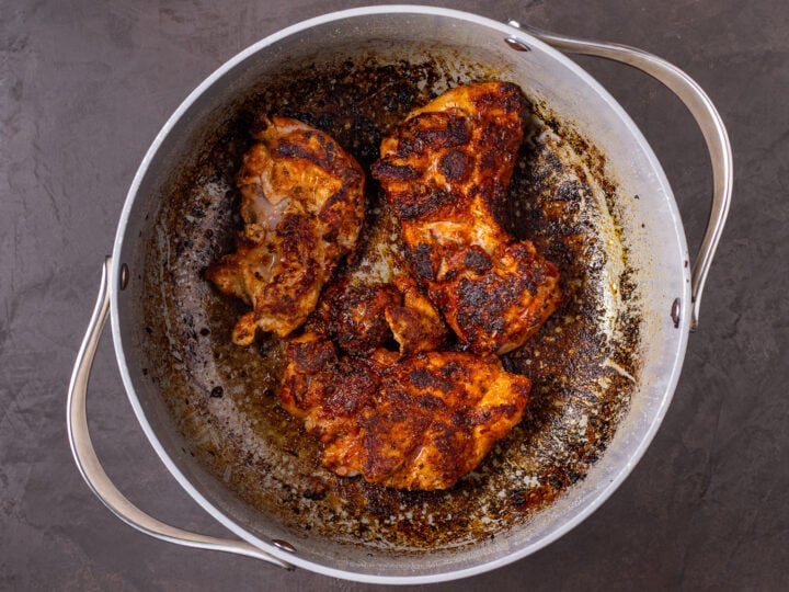 Seasoned chicken thighs seared until deeply browned and caramelized in a large pot.