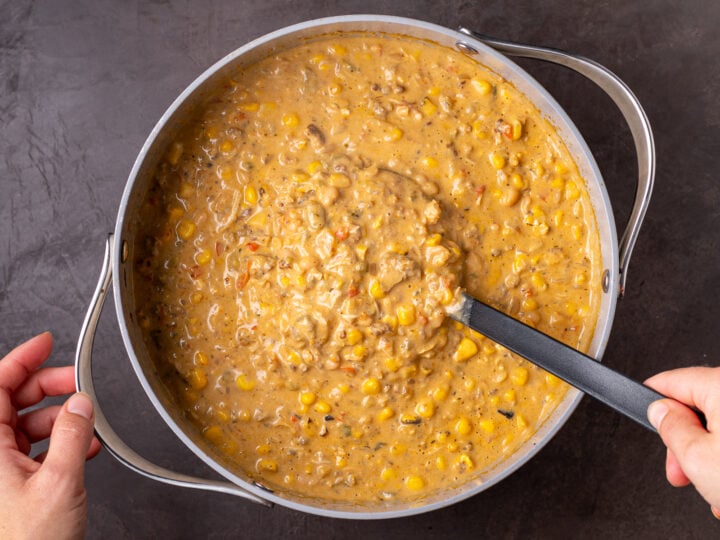 Thick white bean chicken chili with sausage, corn and beans being stirred in a large pot.