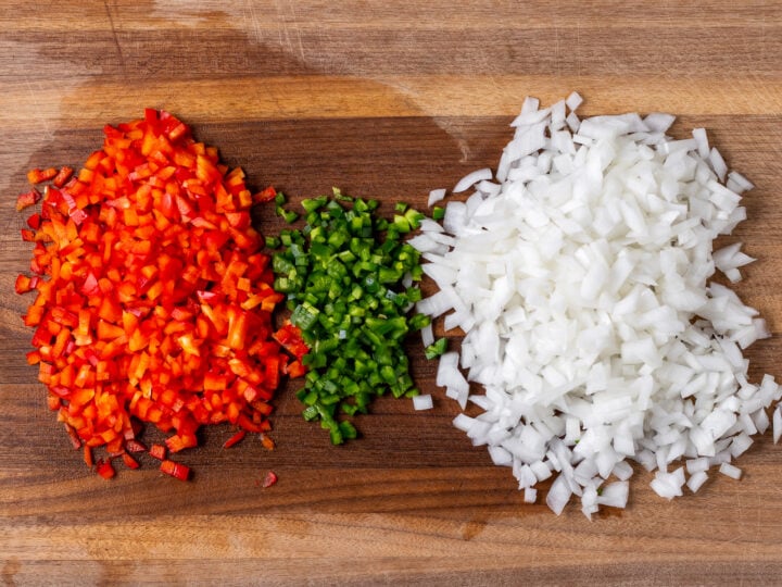 Diced red bell pepper, jalapeño and sweet onion prepped on a wooden cutting board.