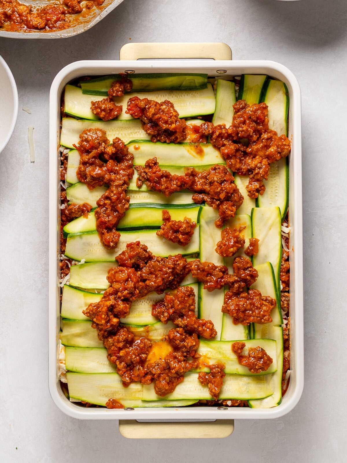 Meat sauce spooned over another layer of zucchini slices during lasagna assembly
