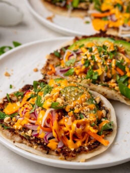 Banh mi smash tacos topped with pickled vegetables, avocado, crushed peanuts, cilantro and sriracha mayo.