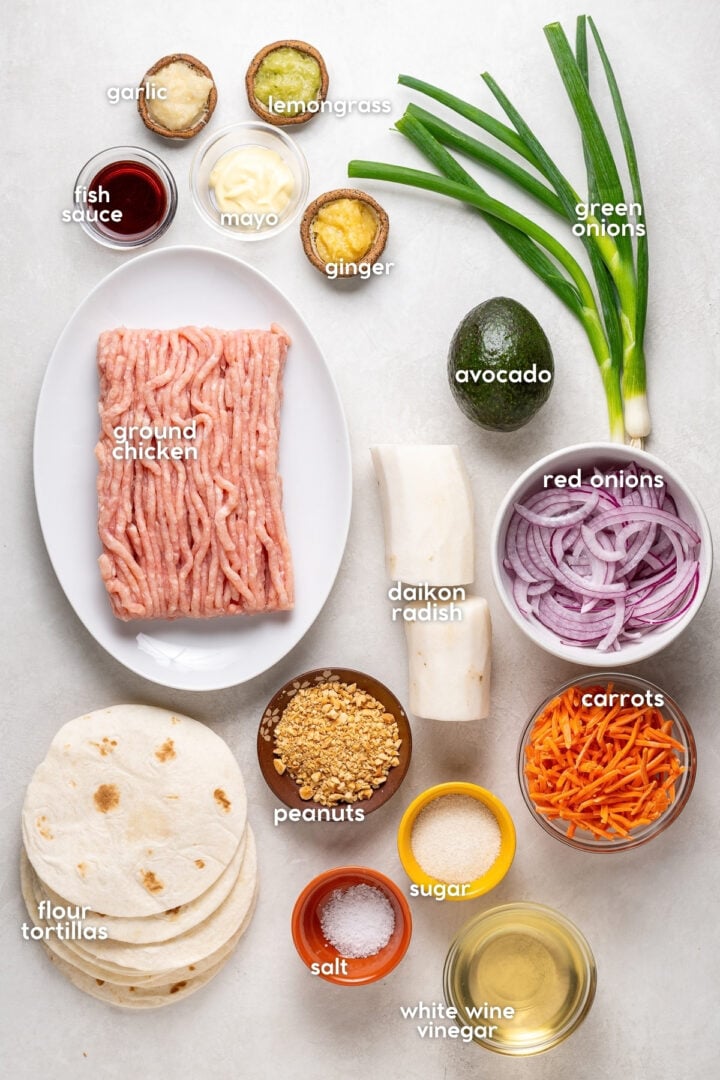 Labeled ingredients for ground chicken banh mi tacos, including tortillas, daikon radish, carrots, vinegar, aromatics and toppings.
