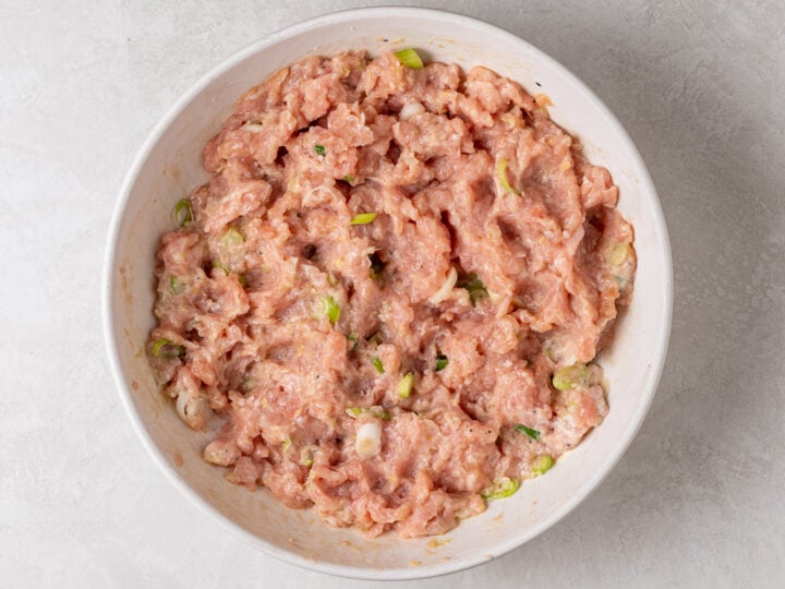 Ground chicken mixture combined with flavor-boosting ingredients by hand in a white mixing bowl.
