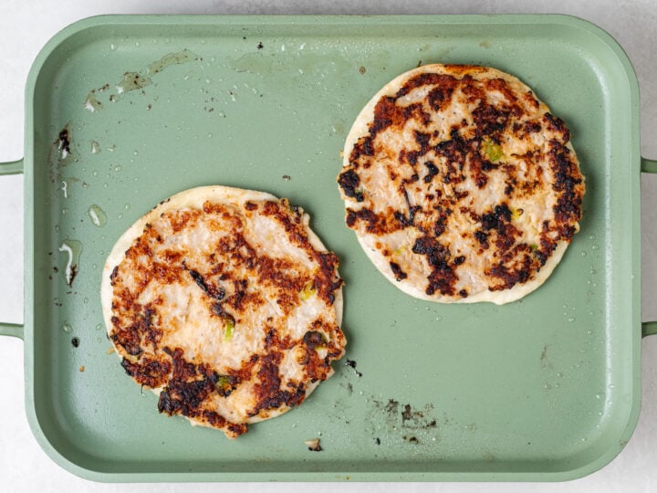 Golden brown ground chicken smash tacos cooking chicken-side up on a green griddle pan.