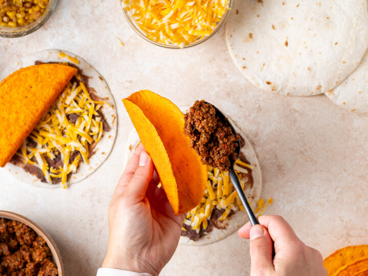 Spoonful of taco meat being added to a nacho cheese crunchy taco shell.