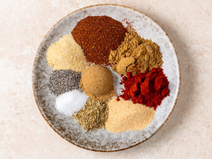Homemade taco seasoning spices arranged on a ceramic plate with brown sugar, including chili powder, garlic powder, and onion powder.