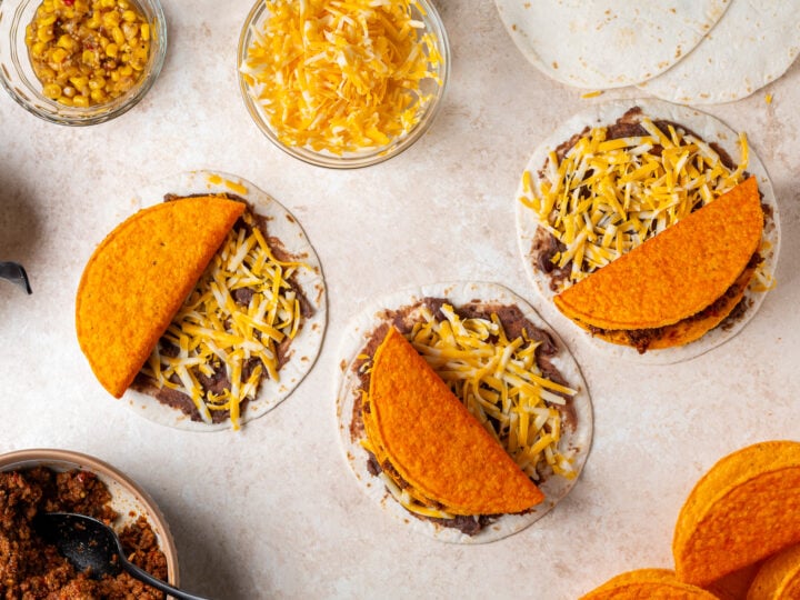 Crunchy taco shells filled with beef placed over half of flour tortillas with refried beans and shredded cheese.