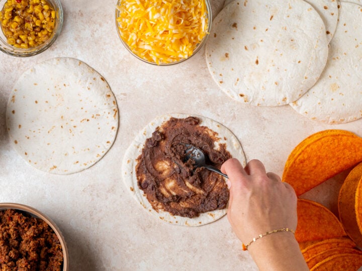 Refried beans being spread onto a small flour tortilla.