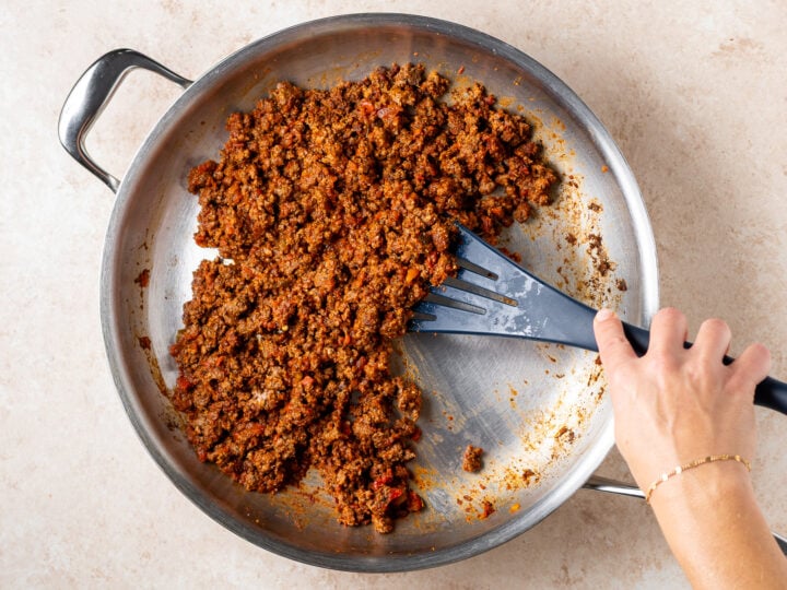 Seasoned ground meat cooking in a stainless steel skillet with a black spatula.
