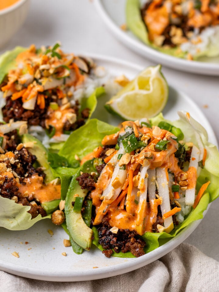 Close-up of gochujang ground beef lettuce wraps with pickled pear slaw, avocado, peanuts and an orange spicy aioli drizzled on top