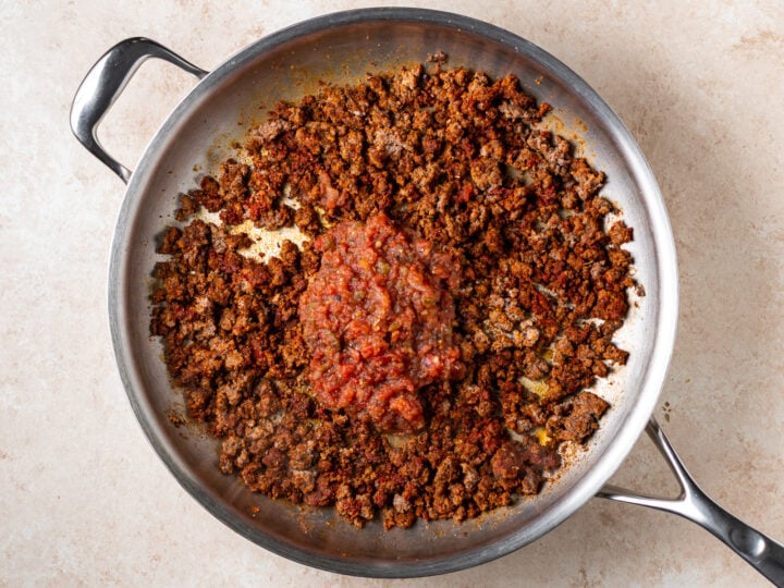 Restaurant-style salsa added to seasoned ground beef in a stainless steel skillet.
