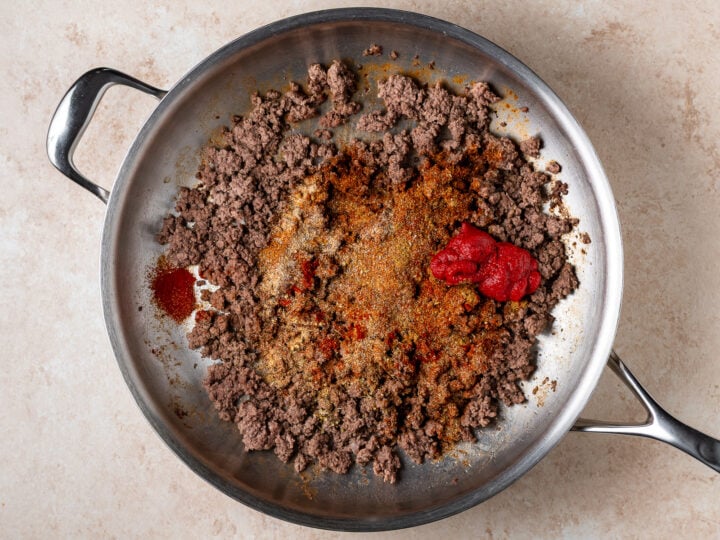 Browned ground beef topped with taco seasoning blend and a dollop of tomato paste in a pan.