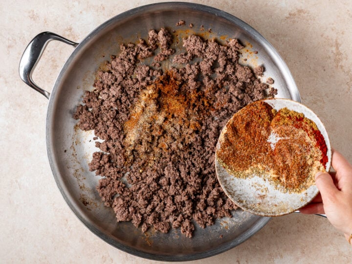 Taco seasoning being sprinkled over 1 lb ground beef cooked in a hot skillet.