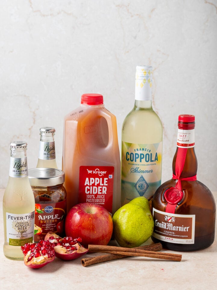 Ingredients for Thanksgiving sangria including white wine, apple cider, Grand Marnier, apple butter, ginger beer, apples, pear, pomegranate and cinnamon sticks.