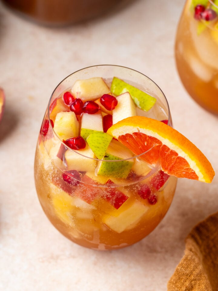 Overhead close-up of fall sangria with chopped apples, pears, pomegranate arils, ice and an orange slice.