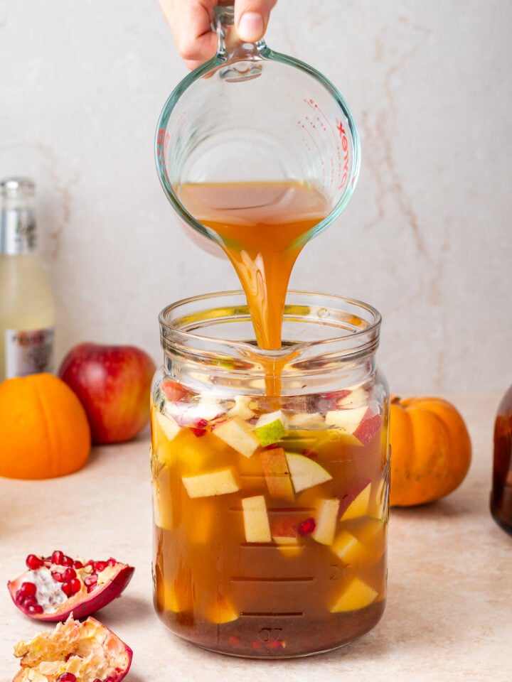 Adding fresh apple cider to a pitcher of white wine, apples, pears and cinnamon for homemade fall sangria.